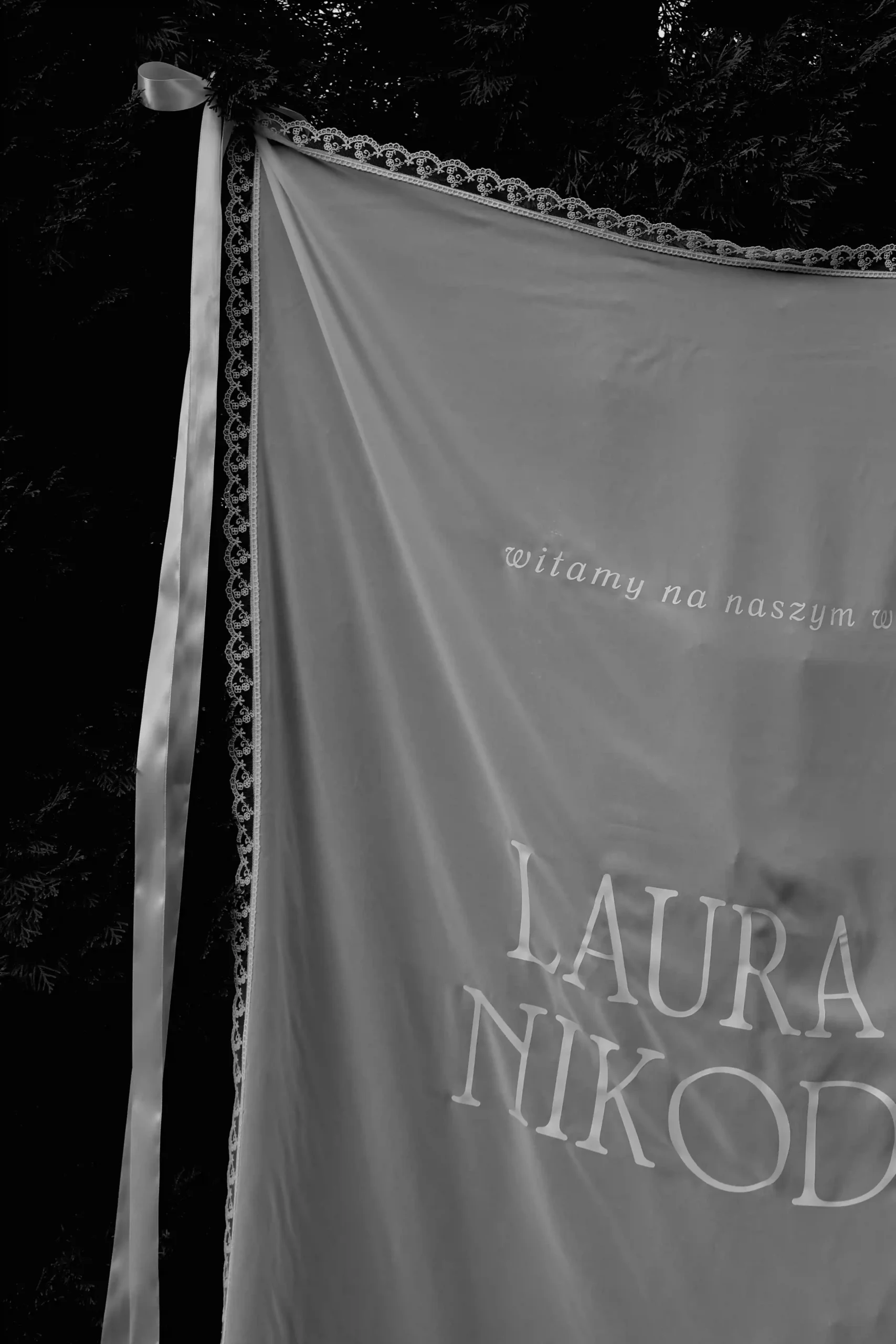 Czarno-białe zdjęcie przezroczystego materiału z koronką i napisami.