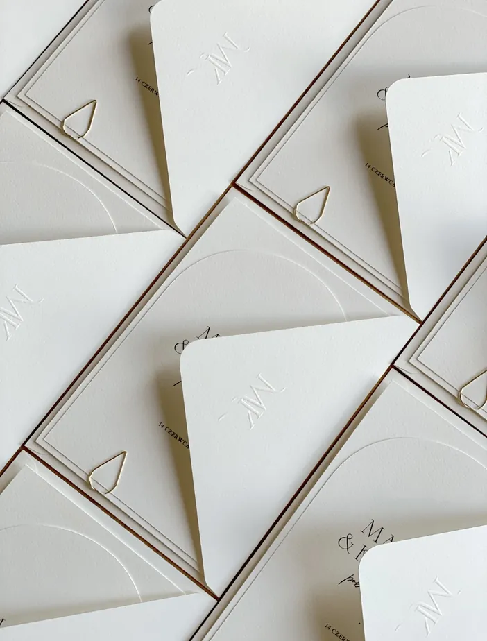 Białe koperty prostokątne ze złotym spinaczem.
