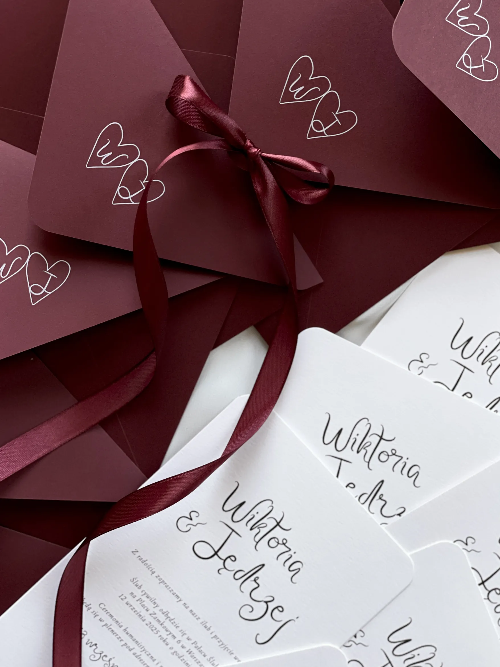 Czerwone kartki papeterii ślubnej z dekoracyjną czcionką w białym kolorze.