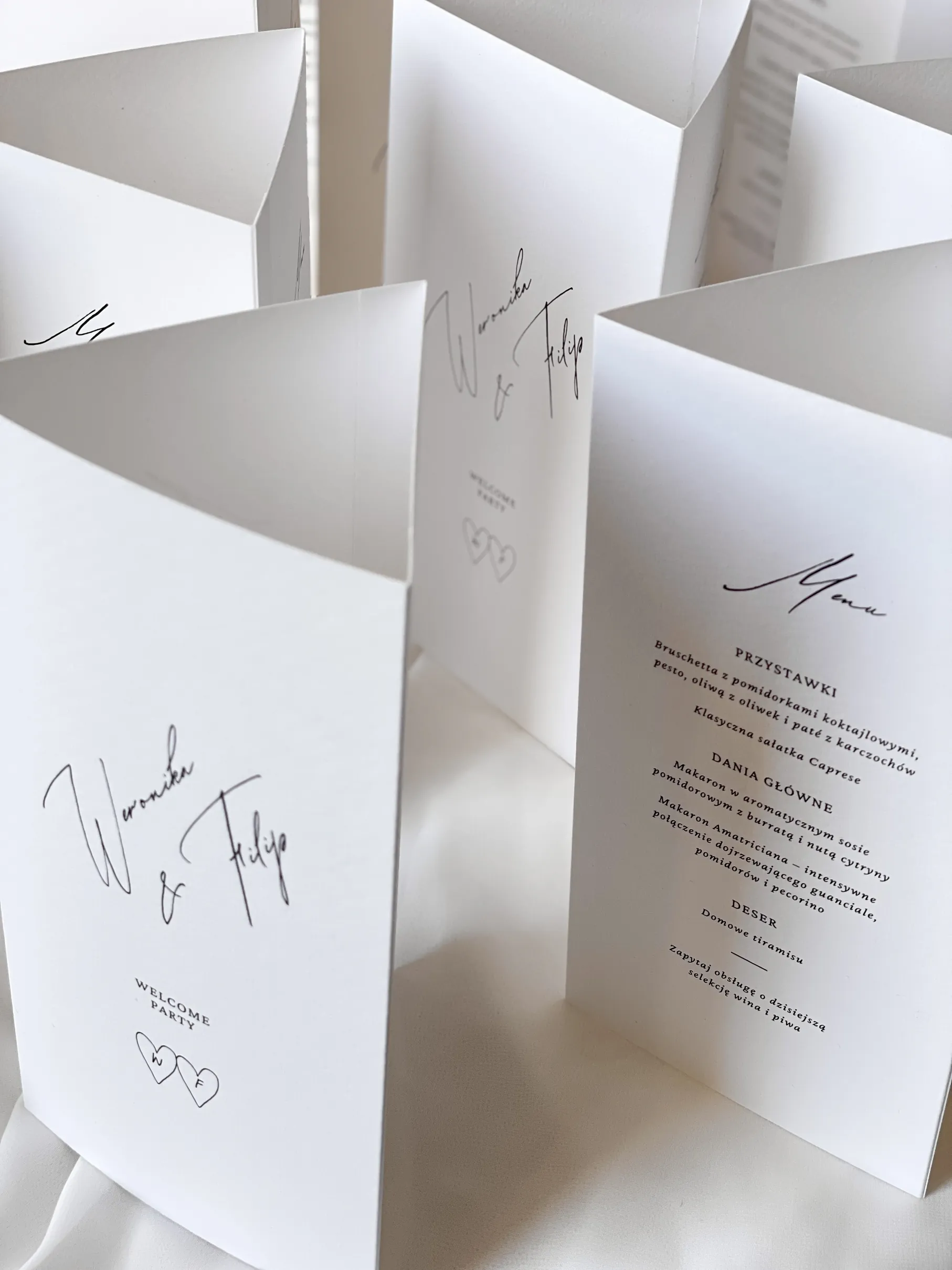 Białe kartki papeterii ślubnej z dekoracyjną czcionką w czarnym kolorze.