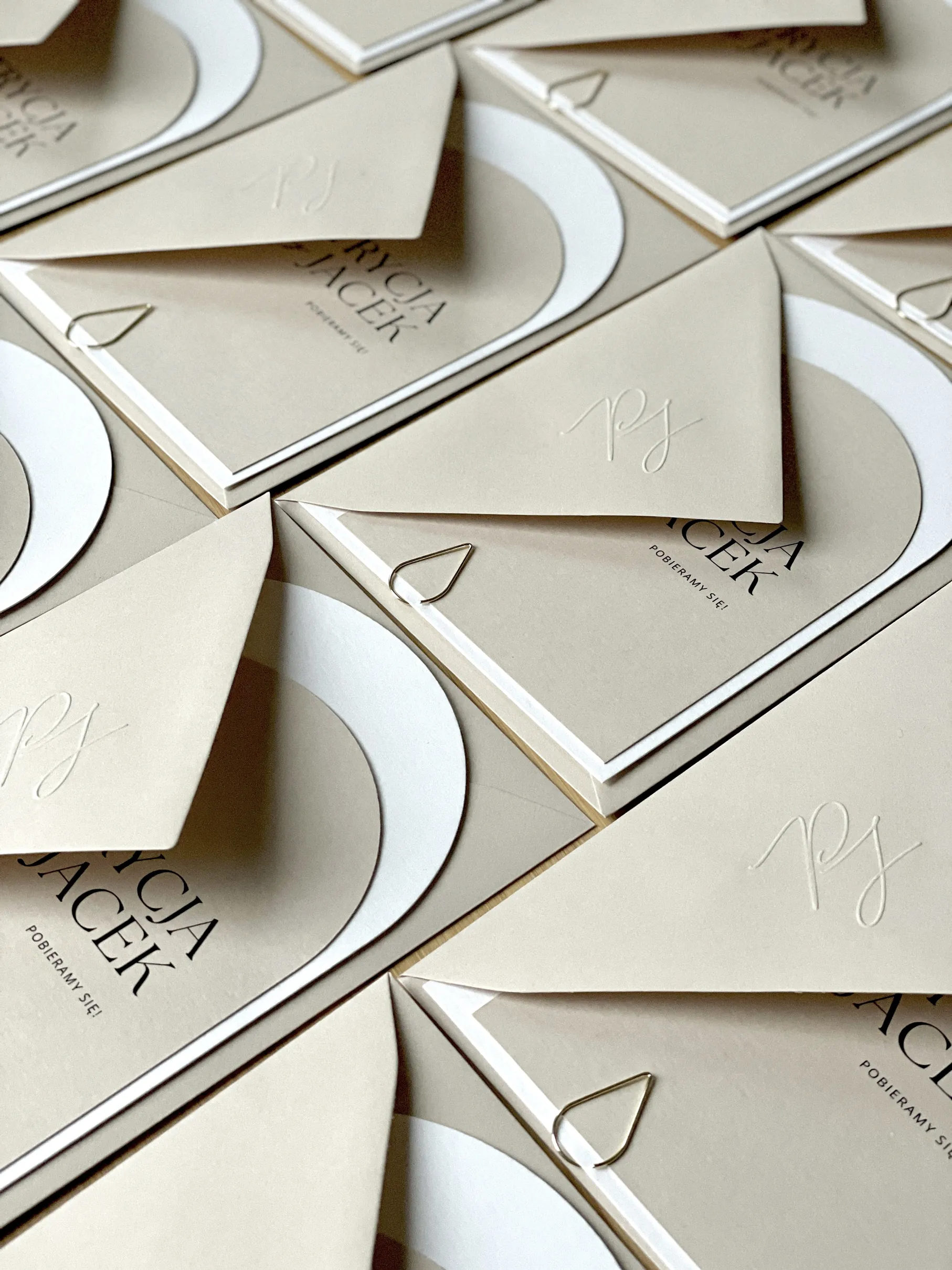 Beżowe kartki papeterii ślubnej z dekoracyjną czcionką w czarnym kolorze.