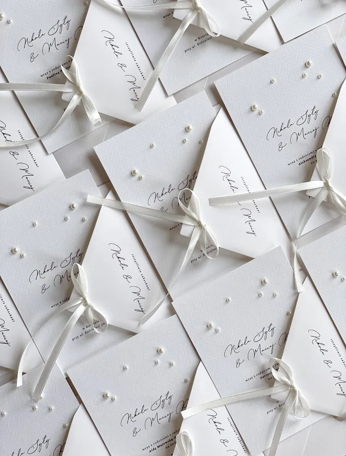 Białe kartki papeterii ślubnej z dekoracyjną czcionką w czarnym kolorze.